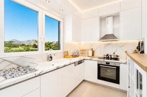 Eine moderne Küche mit weißen Schränken, einem eingebauten Ofen und einem Fenster mit Blick auf die Berge.