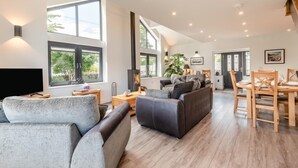 A spacious living room with a fireplace, large windows, and a dining area with wooden furniture. - 3 Bed in Penrith (oc-89427) (Hutton)