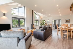 Ein geräumiges Wohnzimmer mit Kamin, großen Fenstern und einem Essbereich mit Holztischen und -stühlen.