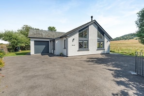 Ein zweistöckiges Gebäude mit Garage, Auffahrt und ländlicher Landschaft im Hintergrund.