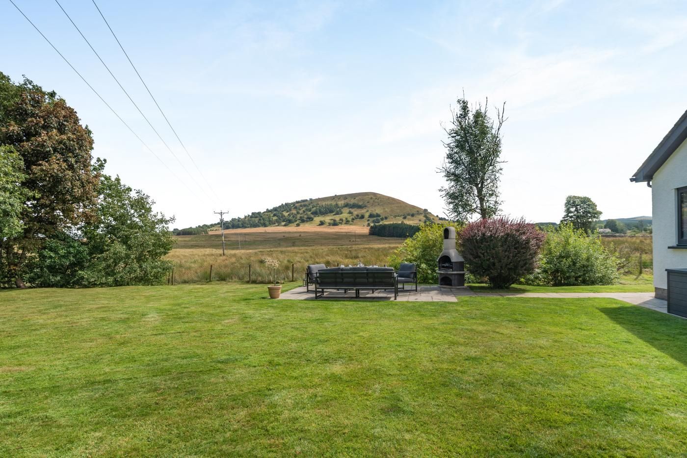 A grassy backyard with a bench, a barbecue grill, and a house in the background.