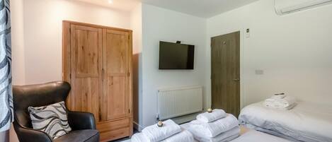 A hotel room with a bed, a chair, a wardrobe, a television, and a radiator.