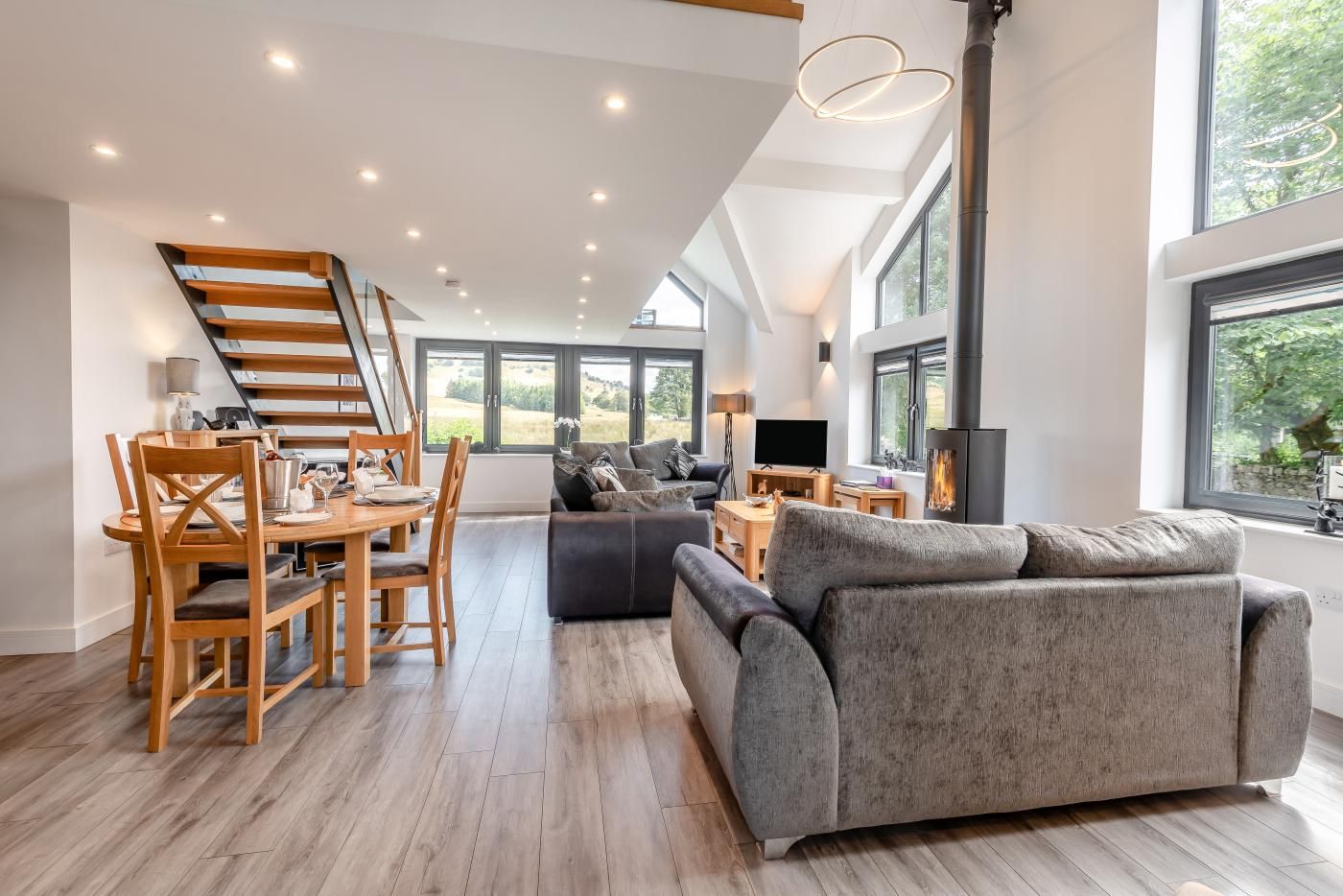 A spacious living area with a modern staircase, a fireplace, and a large window offering a view of the outdoors.