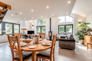 A modern dining area with a wooden table set for a meal, a sofa, and a large window with a view of greenery. - 3 Bed in Penrith (oc-89427) (Hutton)