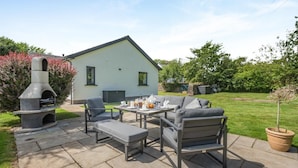 An outdoor patio with a stone fireplace, a dining table set with chairs, and a lawn. - 3 Bed in Penrith (oc-89427) (Hutton)
