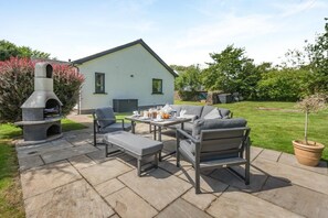 Eine Terrasse im Freien mit einem Steinkamin, einem Esstisch mit Stühlen und einem Rasen.
