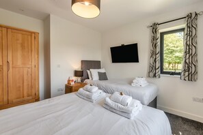 Ein Hotelzimmer mit zwei Betten, einem Kleiderschrank, einem Flachbildfernseher und einem Fenster mit Vorhängen.