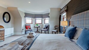 Et hotelværelse med en stor seng, to lænestole, et lille bord med en vase og et vindue med udsigt.
