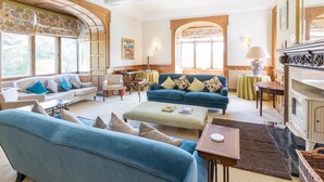 A spacious living room with a fireplace, multiple seating areas, and large windows. - 12 Bed in Tomatin (oc-ca203) (Woodend)