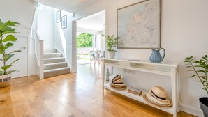 Un intérieur moderne avec un escalier, une console sur laquelle sont posés des chapeaux, et une carte accrochée au mur.