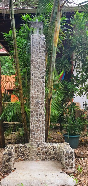 A stone water feature with a cascading design, surrounded by lush greenery and a concrete base. - Tropical Pool Oasis Steps From Beach, Shops, Cafès (Sámara)