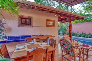 A dining area with a table, chairs, a fan, and a poolside setting. - Tropical Pool Oasis Steps From Beach, Shops, Cafès (Sámara)