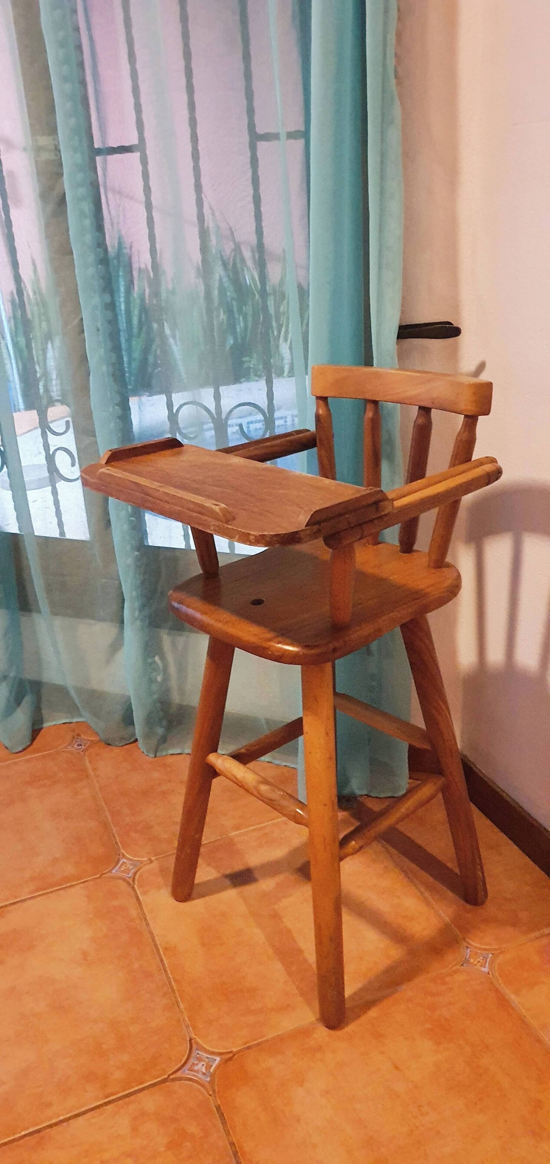 A wooden chair with a tray, positioned in front of a window with curtains.