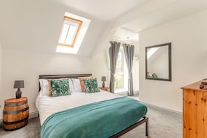 A bedroom with a skylight, a bed with a teal bedspread, a wooden side table, a mirror, and a wooden dresser. - 6 Bed in Holsworthy (oc-s41430) (Holsworthy Hamlets)