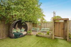 A backyard with a round wicker bed, picnic tables, and a wooden gate. - 6 Bed in Holsworthy (oc-s41430) (Holsworthy Hamlets)