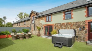 Une maison à deux étages avec une façade en pierre, un jacuzzi et une terrasse aménagée avec du mobilier d’extérieur.