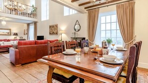 Un vaste espace de vie comprenant un coin repas avec une table préparée pour le petit-déjeuner, un canapé rouge et un lustre.