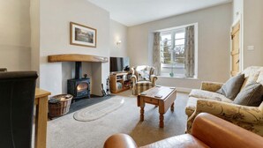 A cozy living room with a fireplace, a sofa, a chair, and a bookshelf. - 2 Bed in Skelwith Bridge (oc-lr128) (Skelwith)