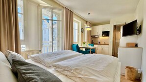 A hotel room with a bed, a small table with a vase, a chair, a TV, and a kitchen area. - Gemutliches Studio in Sellin mit Balkon (Sellin)