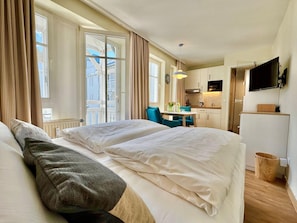 A hotel room with a bed, a small table with a vase, a chair, a TV, and a kitchen area. - Gemutliches Studio in Sellin mit Balkon (Sellin)