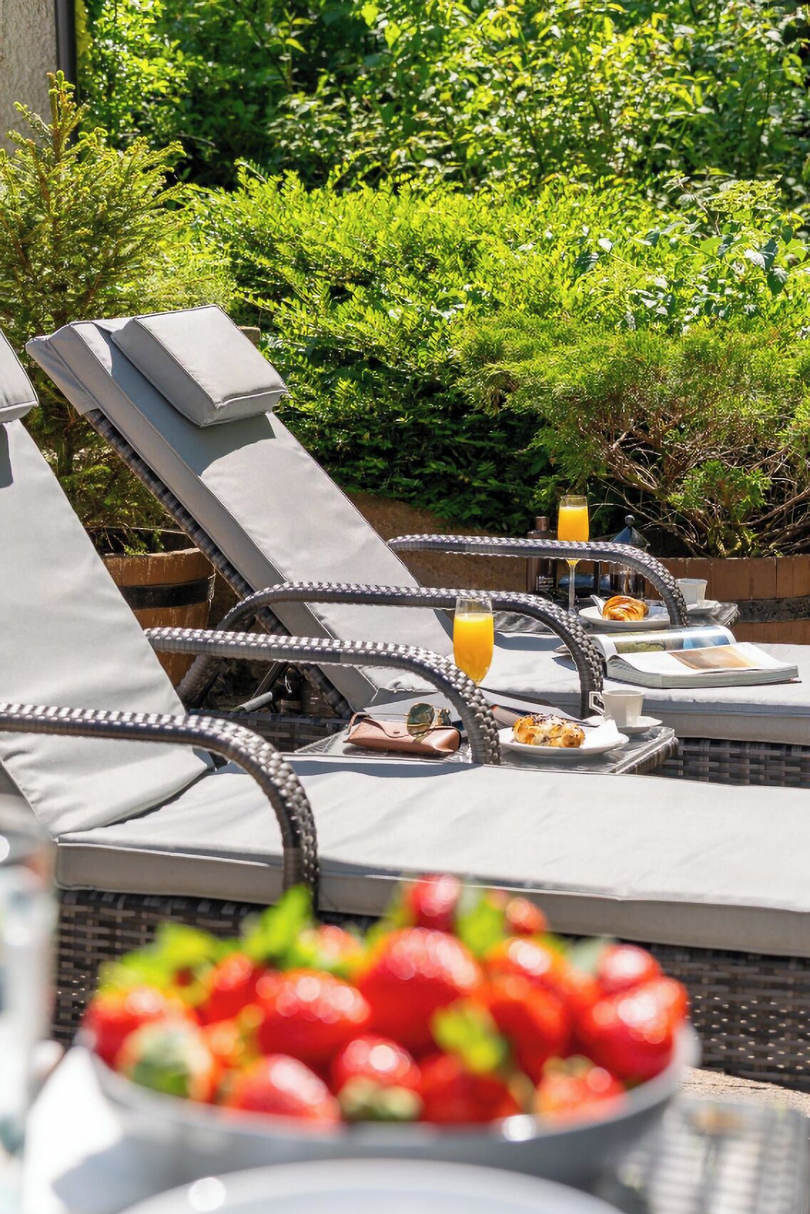 Outdoor lounge chairs with cushions, a table with a drink, and a bowl of fruit.