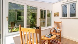 Una stanza con una sedia in legno, un tavolino rotondo e una finestra vista su del verde.