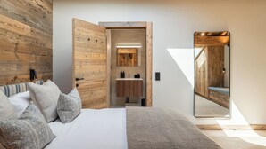 Een slaapkamer met een houten hoofdbord, een bed met kussens met een patroon, een nachtkastje en een spiegel die de kamer weerspiegelt.