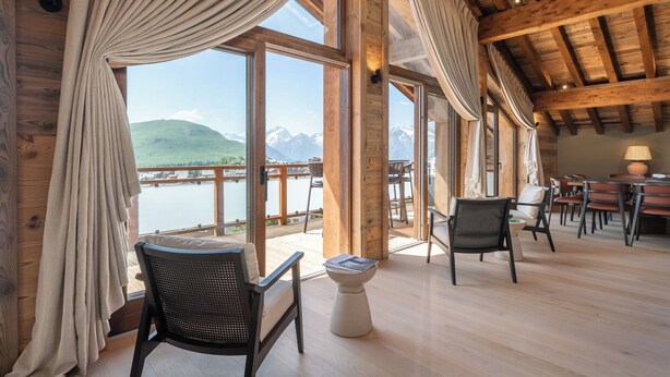 Een houten interieur met grote ramen met uitzicht op een meer en bergen.