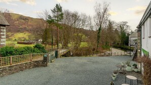 Ein Kieshof mit einer Steinbrücke, ein weißes Gebäude mit Balkon und Blick auf ein Tal mit Bäumen und einem Hügel.