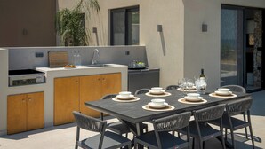 Una cocina al aire libre con una mesa de comedor preparada para seis personas, rodeada de sillas.