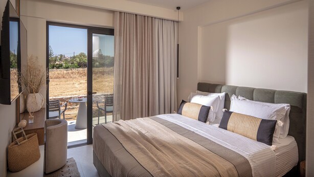 Un dormitorio con cama, televisor, vista al exterior y puerta corrediza.
