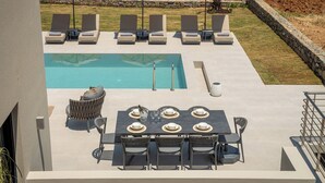 Un área junto a la piscina con sillones reclinables, una mesa de comedor y sombrillas.