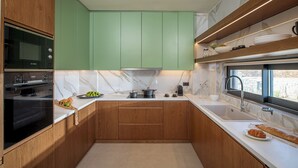Una cocina compacta con microondas, horno, armarios verdes, encimera de mármol y ventana con vistas.