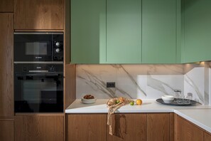 Eine Küche mit Bosch-Ofen, Holzschränken, einer Marmor-Spritzschutzwand und einer Arbeitsplatte mit Obstschale und Gläsern.