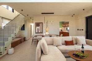 Ein modernes Wohnzimmer mit einer Glasstiege, einer Sofagarnitur, einem Essbereich und einer Küche im Hintergrund.