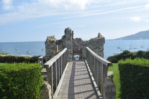 A stone pathway leading to a historic stone structure with a view of the sea and boats. - 3 Bed in Piddlehinton (oc-c40254) (Piddlehinton)