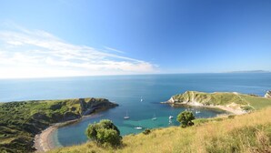 Eine Küstenlandschaft mit klarem Himmel, einer Bucht mit Booten und grasbewachsenen Hügeln.