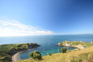 A coastal landscape with clear skies, a bay with boats, and grassy hills. - 3 Bed in Piddlehinton (oc-c40254) (Piddlehinton)