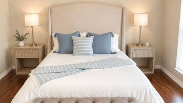 A bedroom with a large bed, two bedside tables with lamps, a bench at the foot of the bed, and a window on the right.