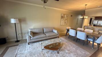A living room with a sofa, coffee table, dining table, chairs, and a ceiling fan.