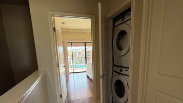 A laundry room with a washing machine and dryer, a door leading to a balcony, and a tiled floor.