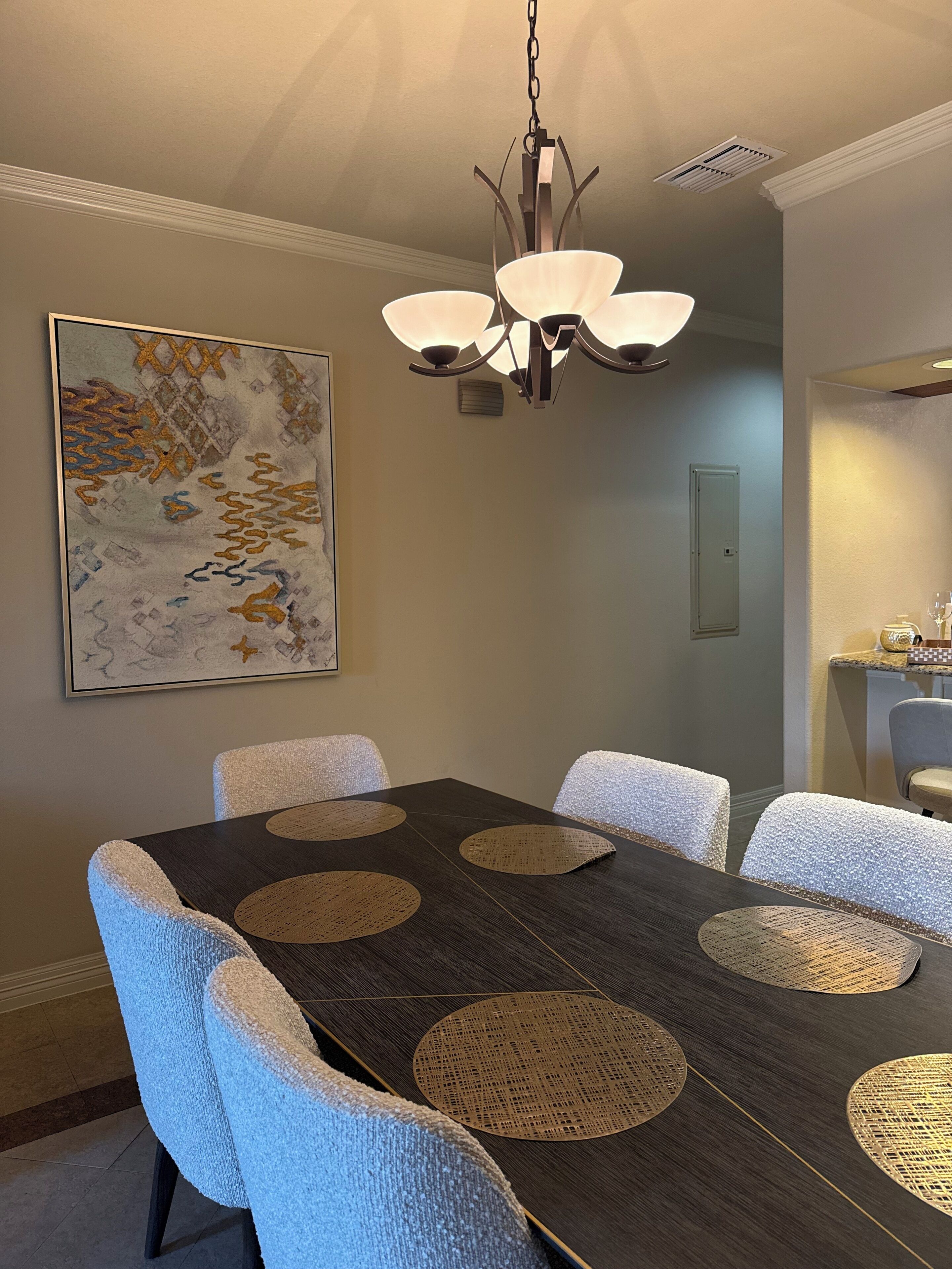 Un coin repas avec une table en bois foncé, des chaises blanches à texture particulière, un luminaire suspendu et un grand tableau abstrait accroché au mur.