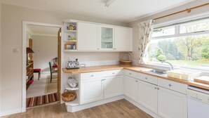 A kitchen with white cabinets, a wooden countertop, a window with a view of trees, and a door leading to a dining area. - 3 Bed in Tomatin (oc-ca211) (Inverbrough)
