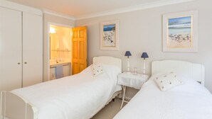 A room with two single beds, a small bedside table with lamps, a bathroom with a mirror and sink, and framed beach paintings on the wall. - 3 Bed in Tomatin (oc-ca211) (Inverbrough)