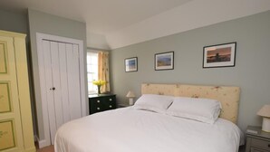 Une chambre à coucher comprenant un lit, une table de chevet, une commode, une porte et deux tableaux encadrés accrochés au mur.