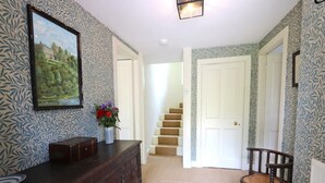 Un couloir avec un papier peint à motifs, une commode en bois, une chaise, un escalier et une porte.