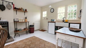 Une cuisine équipée d’une cuisinière, d’un réfrigérateur et d’un évier. On y trouve des étagères remplies d’ustensiles de cuisine et une horloge au mur.