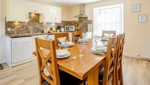 Comedor con una mesa de madera dispuesta para cuatro personas, rodeada de sillas. Zona de cocina con armarios blancos y un microondas.