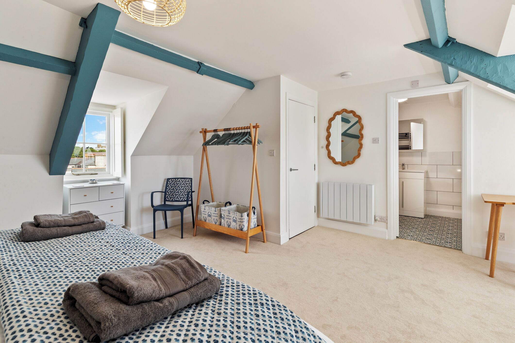 Une chambre à coucher avec un lit, une chaise, un étendoir à linge et une salle de bain visible à travers une porte ouverte.