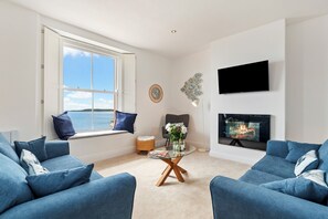 Ein Wohnzimmer mit einer Couch, einem Glastisch, einem Kamin, einem Fernseher und einem Fenster mit Aussicht.